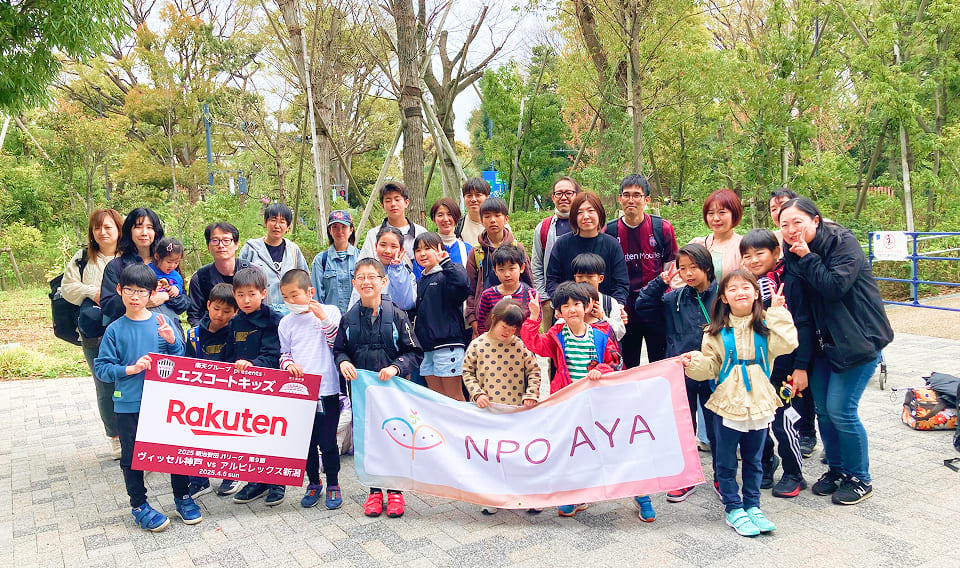 NPO AYAの旗を持つ子どもたちとボランティアの集合写真(社員ボランティアのイメージ)
